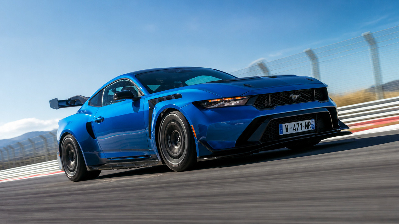 Carro esportivo azul Ford Mustang em alta velocidade em pista de corrida sob céu azul.