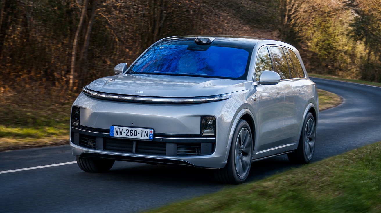 Carro elétrico SUV prata moderno em estrada sinuosa cercada por árvores e vegetação.