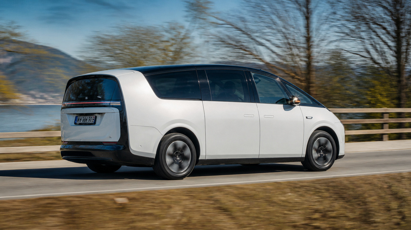 Carro elétrico branco em movimento numa estrada com árvores e montanhas ao fundo.