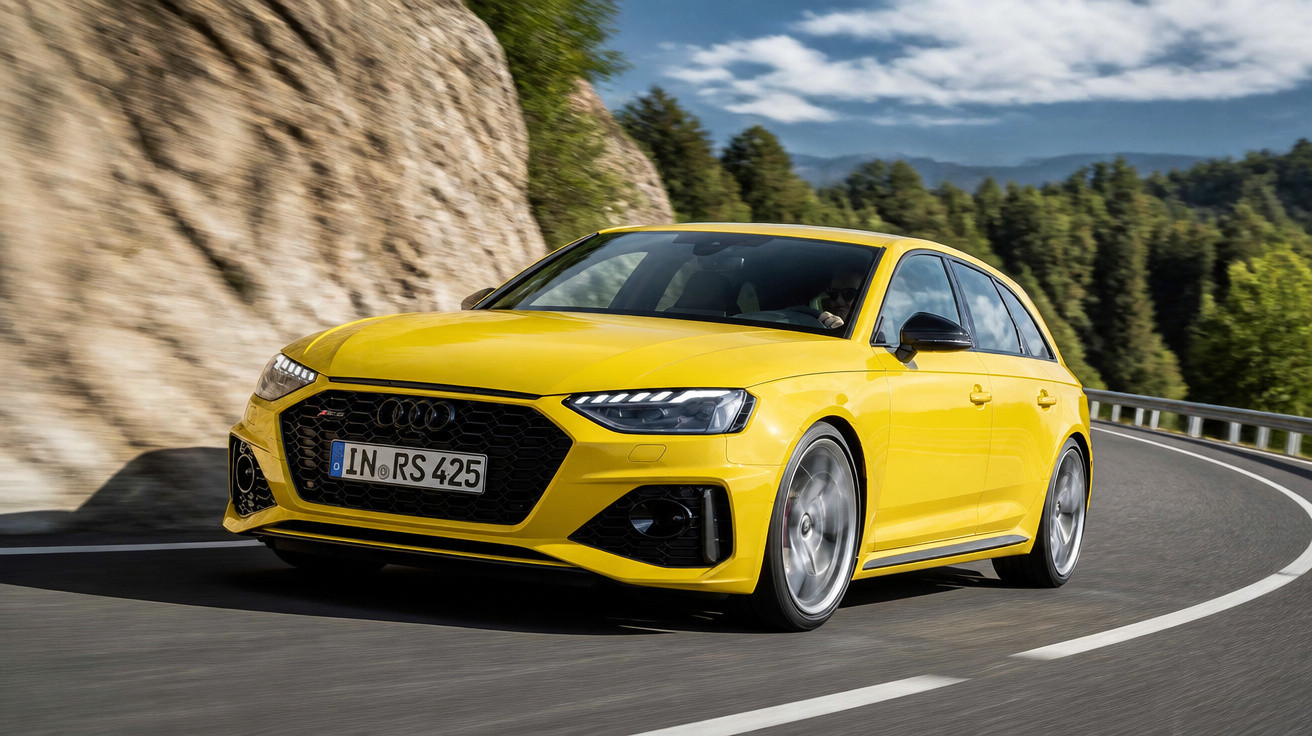 Carro esportivo amarelo Audi RS 4 dirigindo em estrada sinuosa com montanhas e árvores ao fundo.