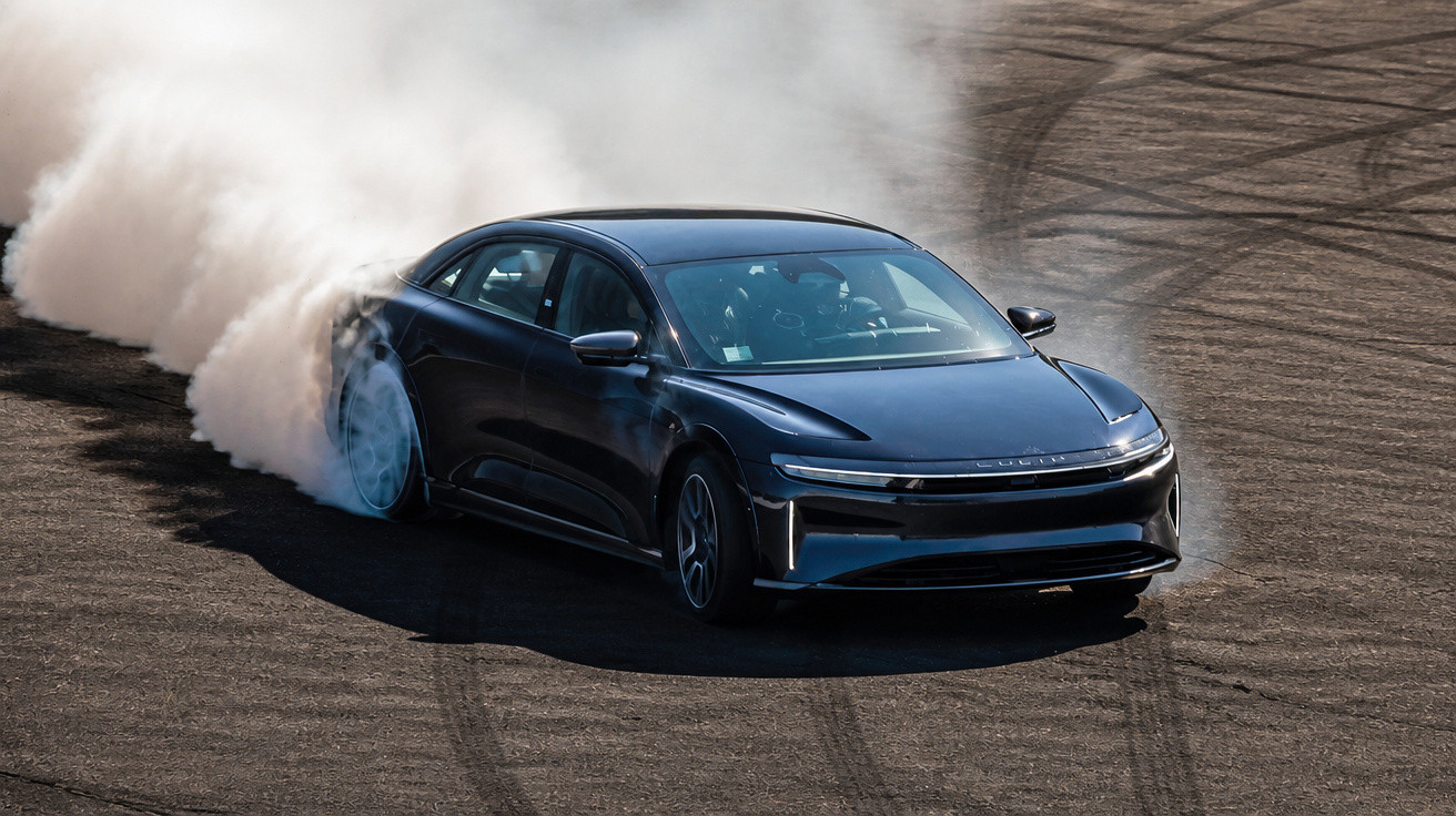 Carro preto fazendo drift em pista de corrida, com fumaça saindo dos pneus traseiros.