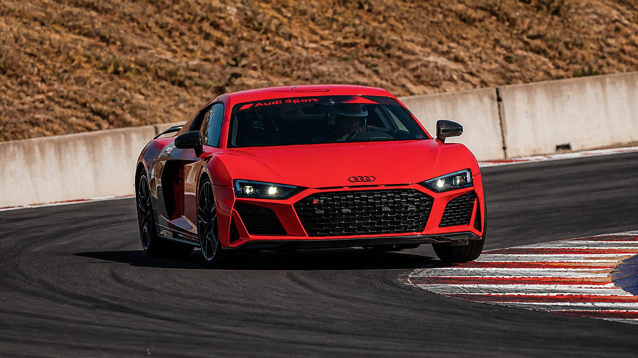 Carro esportivo vermelho Audi R8 fazendo curva em pista de corrida asfaltada em dia ensolarado.