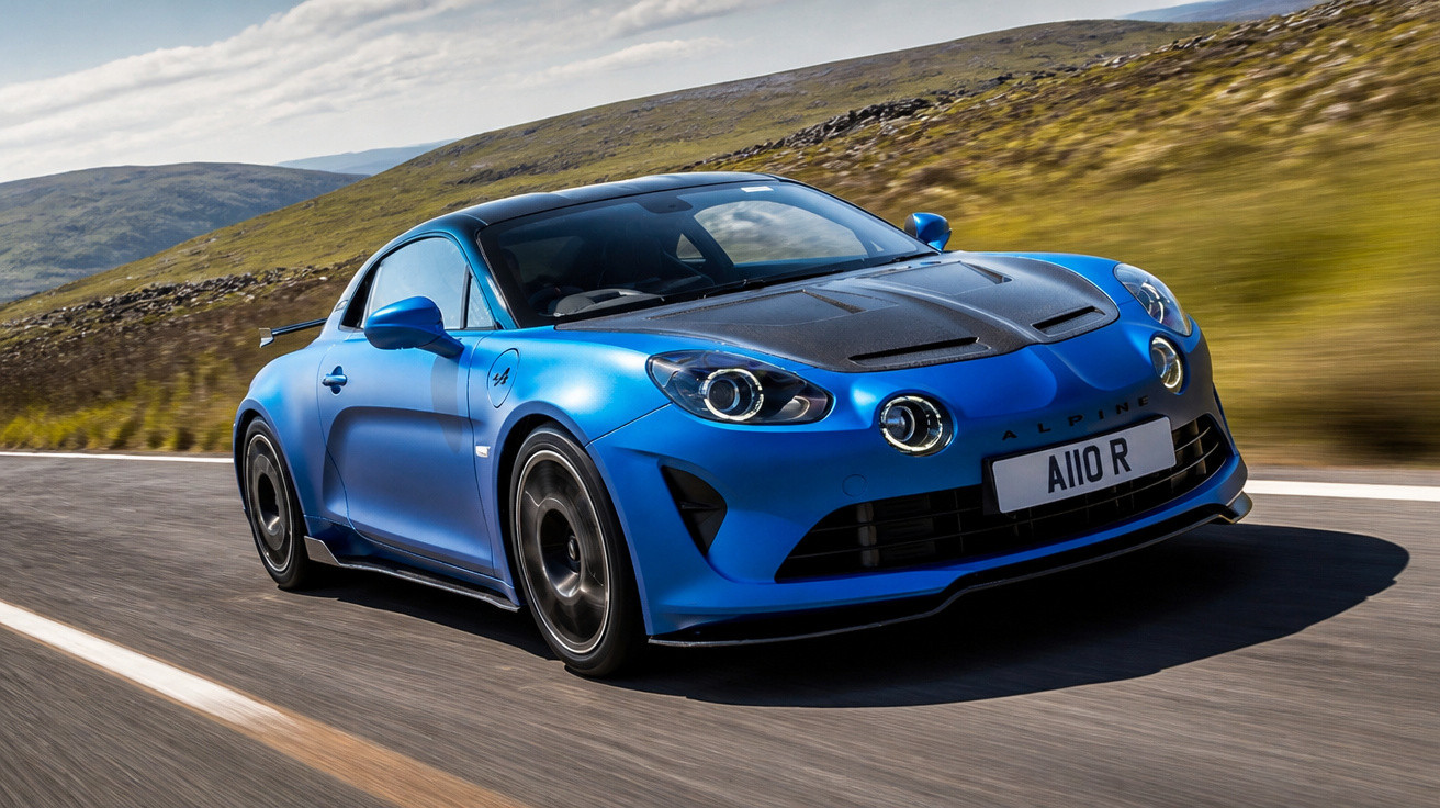 Carro esportivo azul Alpine A110 R em movimento em estrada entre montanhas e céu nublado.