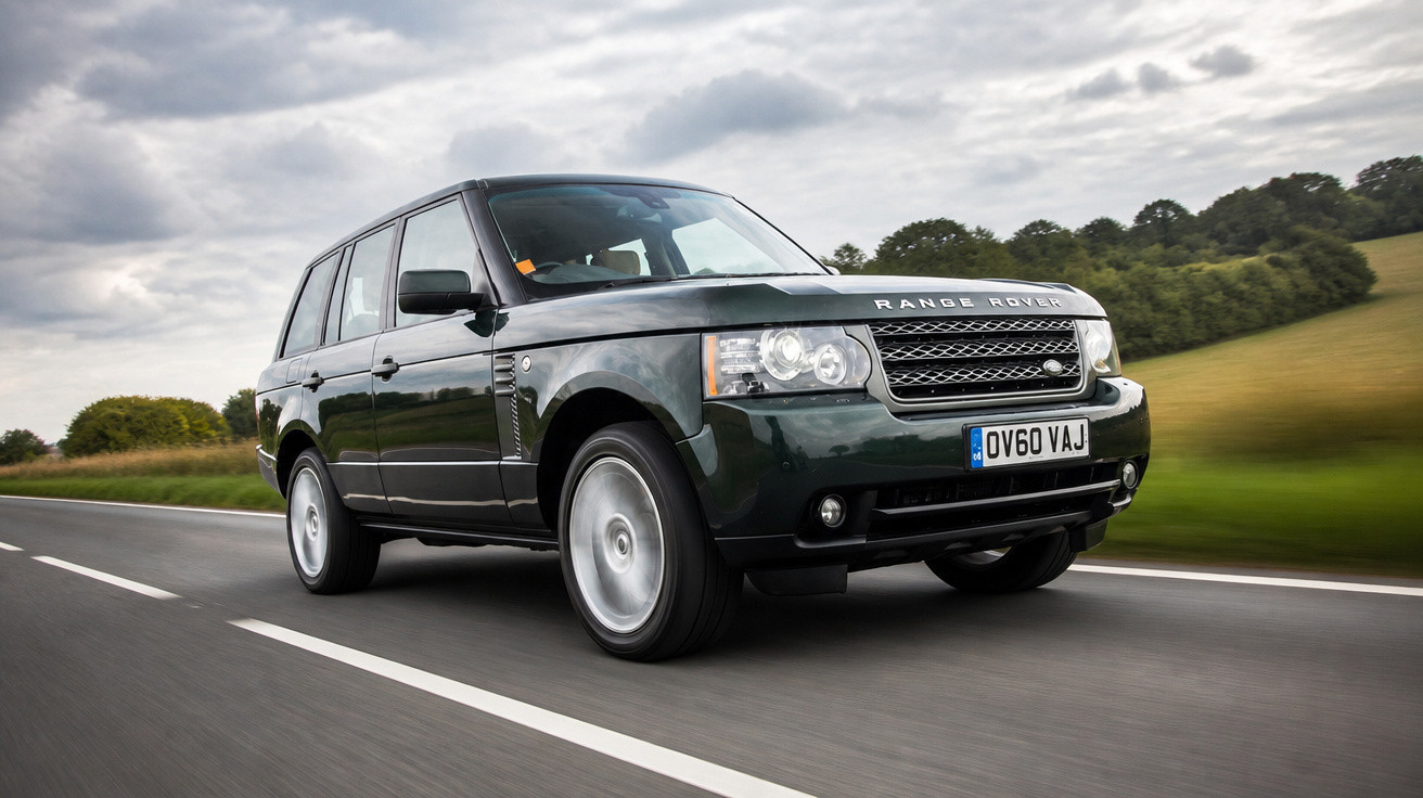 SUV Range Rover preto em movimento em estrada asfaltada com campo e céu nublado ao fundo.
