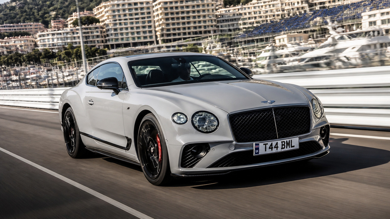 Carro esportivo branco Bentley em alta velocidade em estrada com prédios ao fundo.