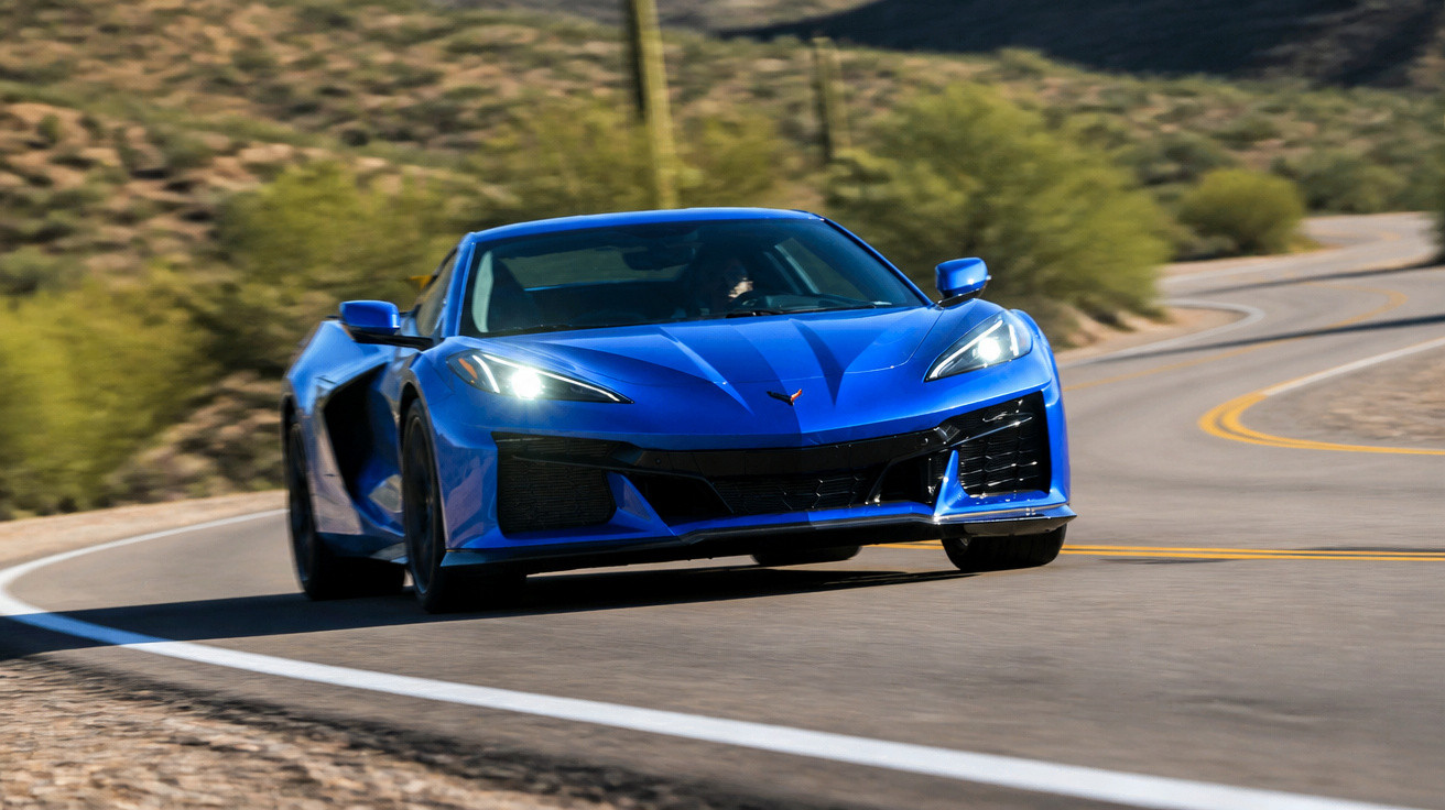 Carro esportivo azul acelerando em estrada sinuosa com paisagem árida ao fundo.