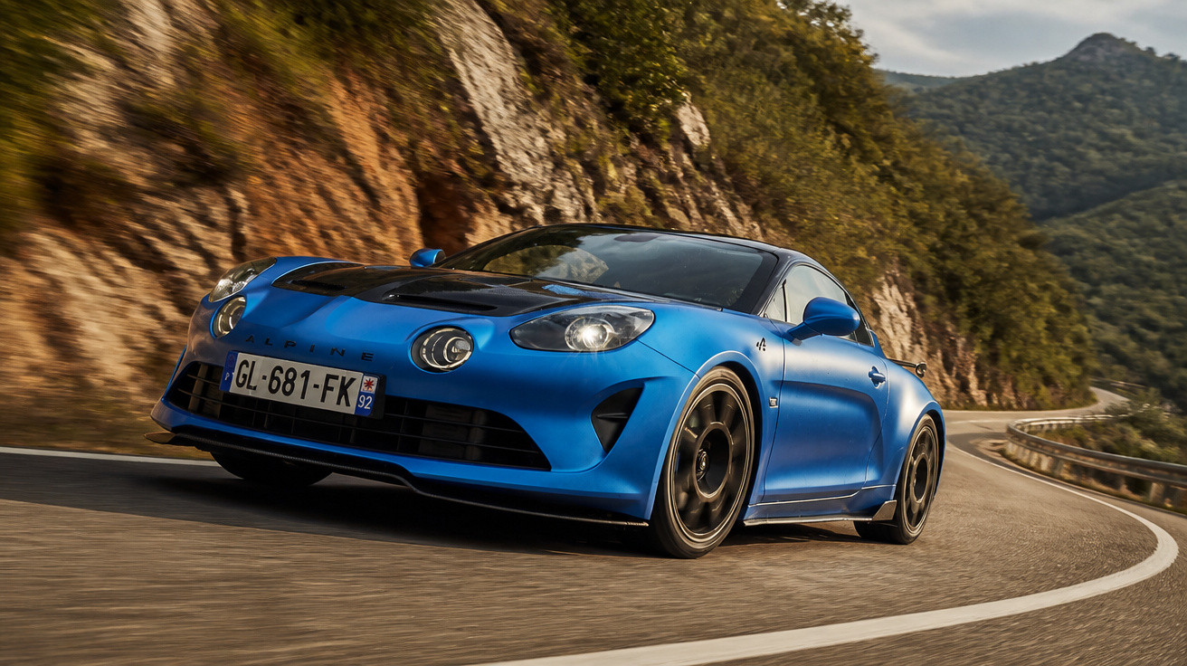 Carro esportivo azul em uma estrada sinuosa rodeada por montanhas e vegetação.