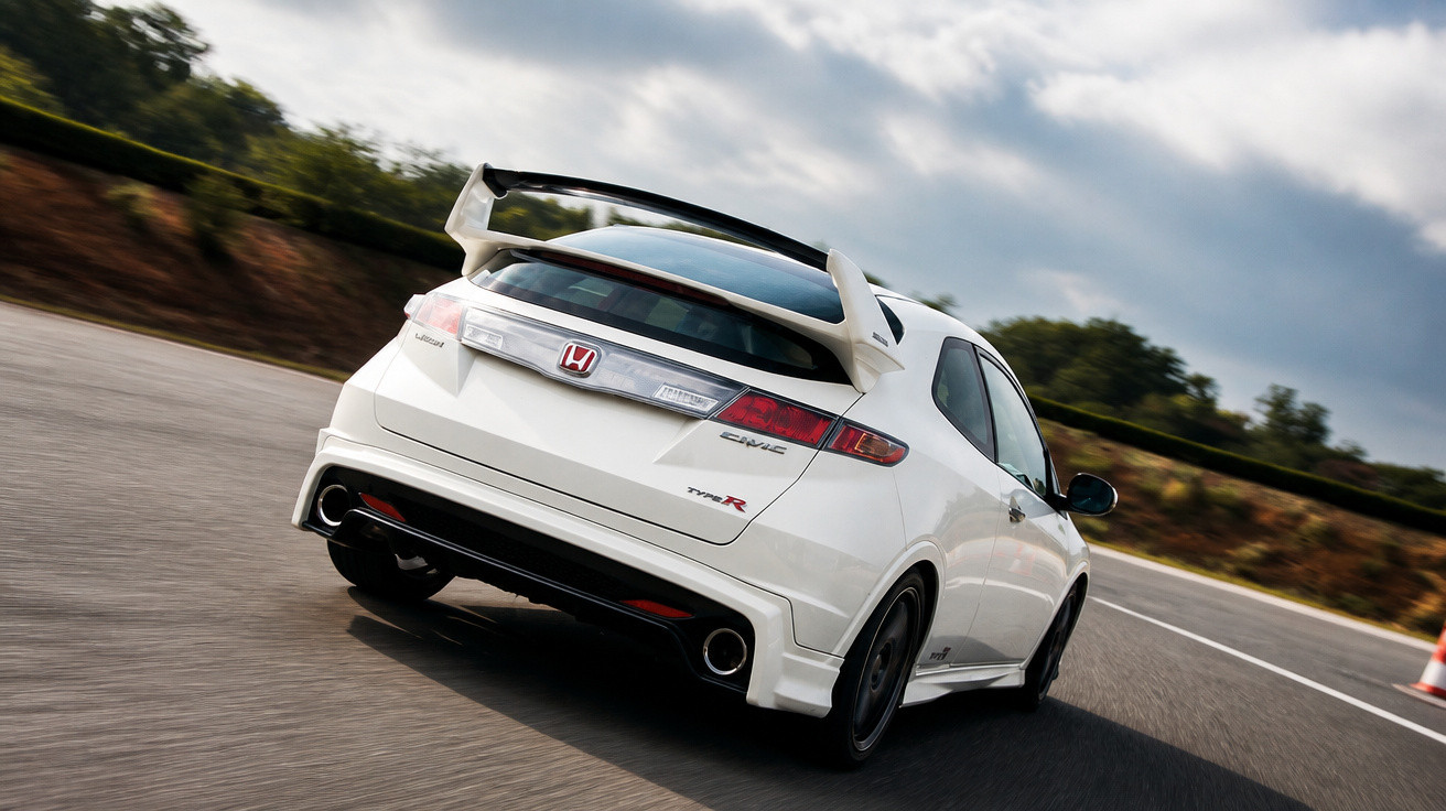 Carro branco Honda Civic Type R em alta velocidade em pista de corrida sob céu nublado.