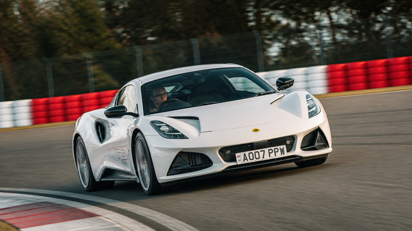 Carro esportivo branco em alta velocidade fazendo curva em pista de corrida com barreira vermelha e branca.