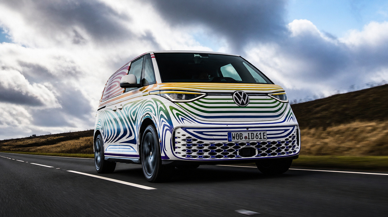 Van elétrica Volkswagen com pintura colorida em linhas curvas circulando em estrada sob céu nublado.