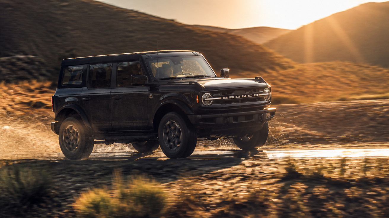 SUV preto Ford Bronco em movimento na estrada de terra ao pôr do sol no deserto.