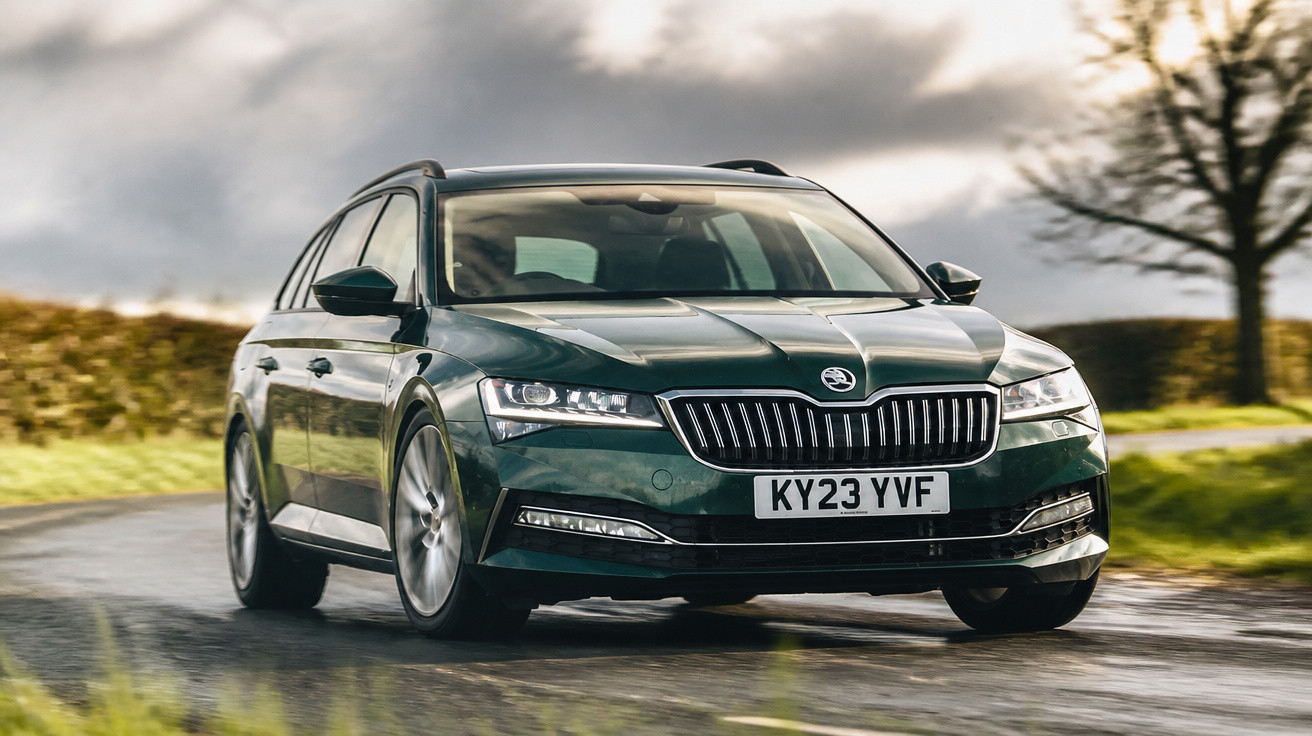 Carro verde escuro Skoda em estrada molhada com céu nublado e árvores ao fundo.