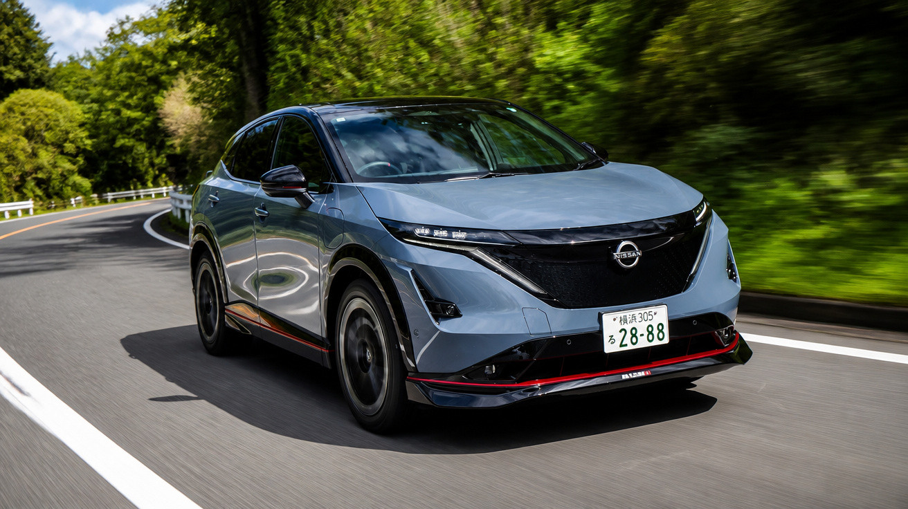 Carro elétrico cinza Nissan cruzando estrada sinuosa cercada por árvores verdes sob céu azul.