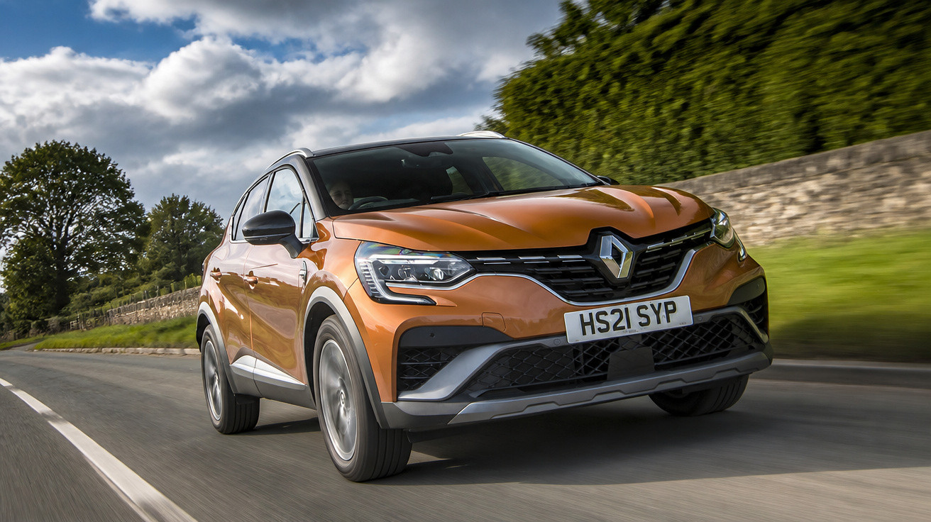 Carro SUV Renault laranja em movimento em estrada com céu nublado e vegetação ao redor.
