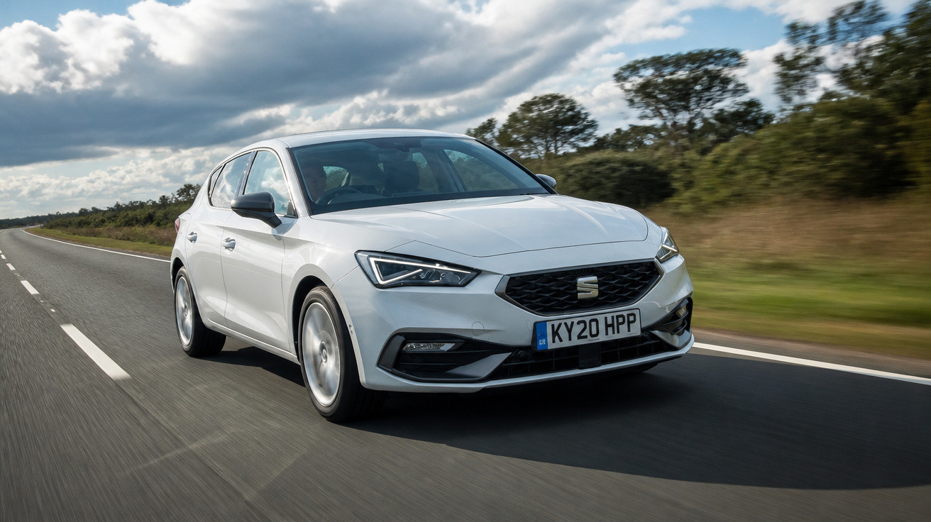 Carro branco modelo hatchback em alta velocidade em estrada reta com céu nublado e árvores ao fundo.