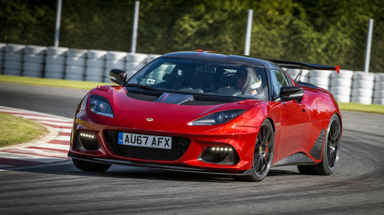 Carro esportivo vermelho em alta velocidade contornando curva em autódromo com motorista usando capacete.