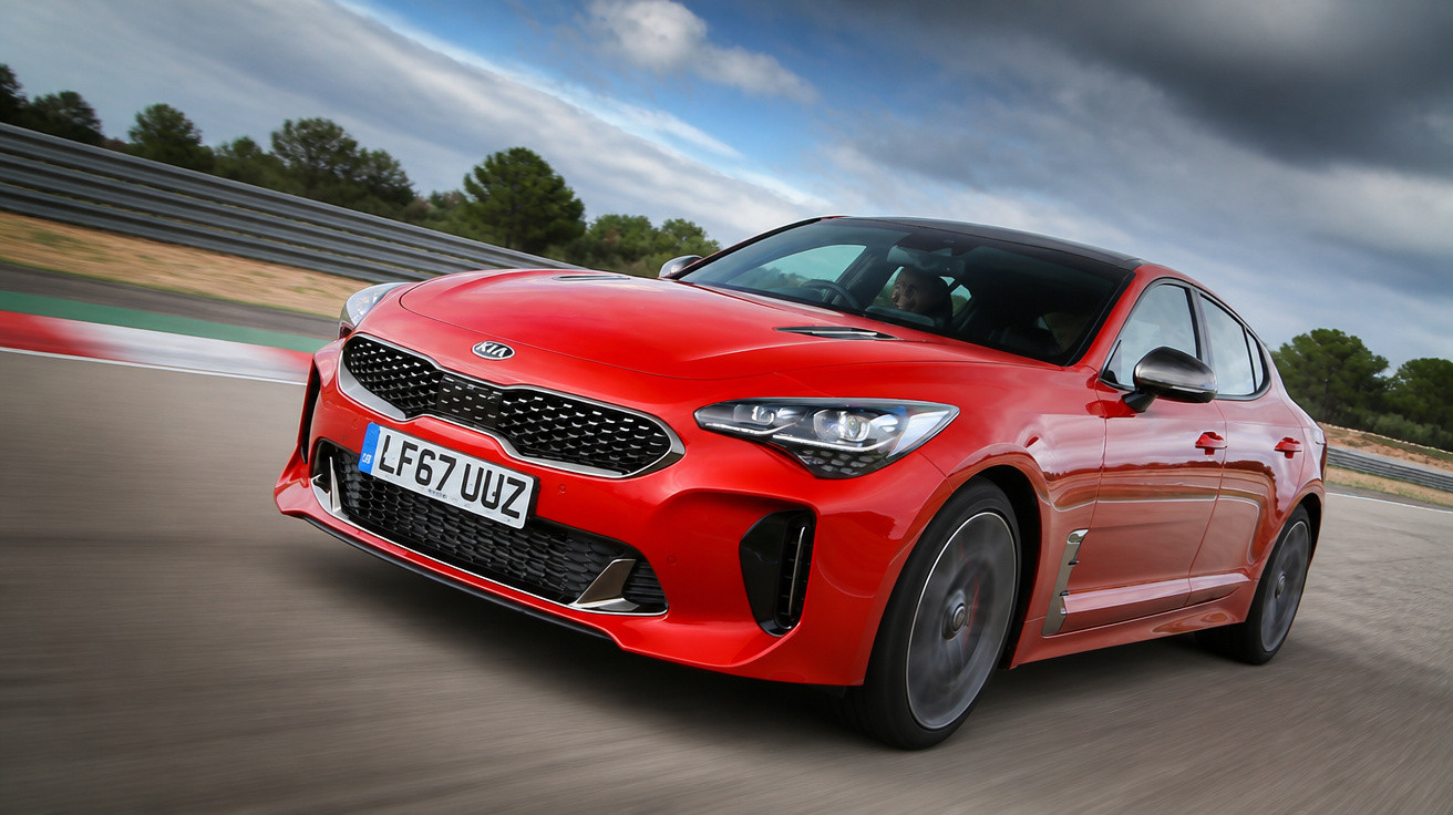 Carro esportivo vermelho da Kia acelerando em pista curva com céu nublado ao fundo.