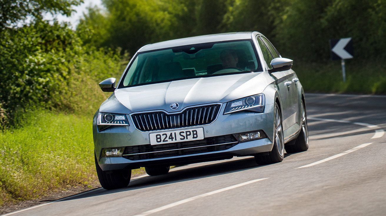 Carro prata Skoda circulando em estrada sinuosa com vegetação ao redor em dia ensolarado.