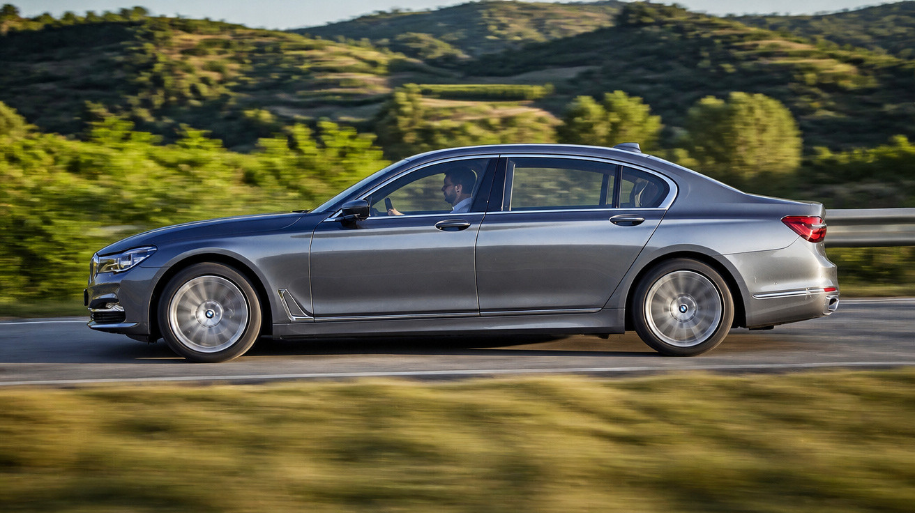 Carro sedan cinza em movimento pela estrada com vegetação e colinas ao fundo.