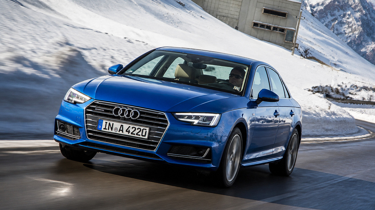 Carro azul Audi sedan em estrada molhada com neve nas montanhas ao fundo.