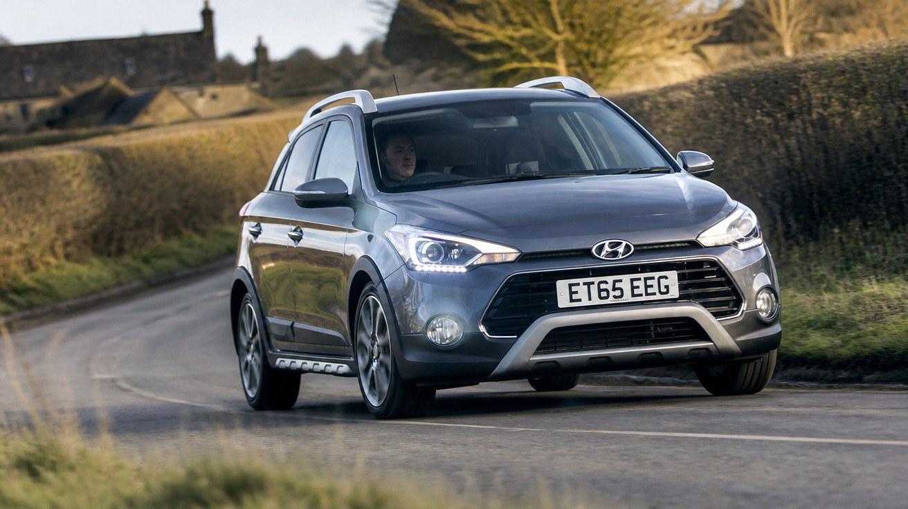 Carro cinza Hyundai em estrada rural com motorista ao volante em dia claro.