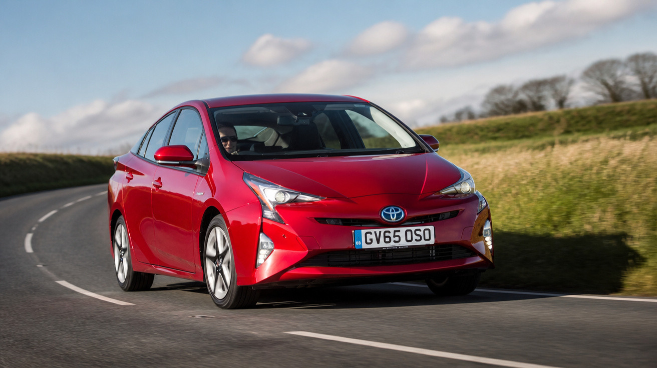 Carro híbrido vermelho Toyota Prius em estrada curva com paisagem rural ao fundo.