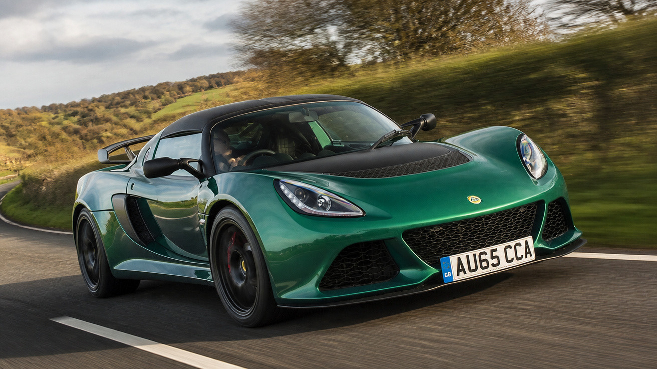 Carro esportivo verde Lotus acelerando em estrada asfaltada com vegetação ao redor em dia nublado.