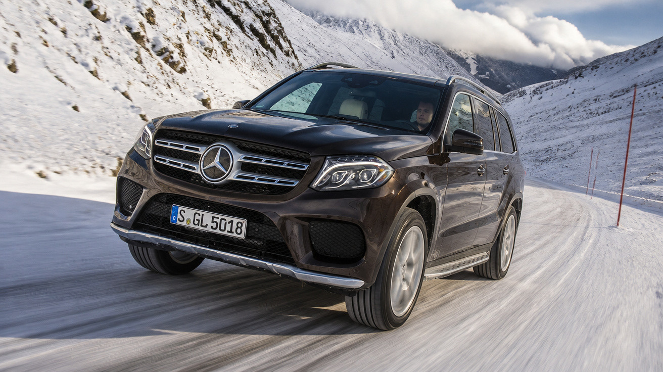 SUV Mercedes-Benz preto dirigindo em estrada coberta de neve entre montanhas nevadas.