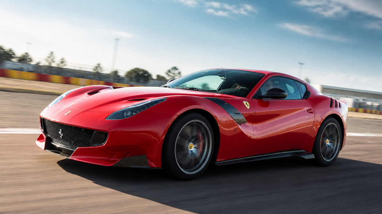 Carro esportivo vermelho Ferrari em alta velocidade em pista de corrida sob céu azul.