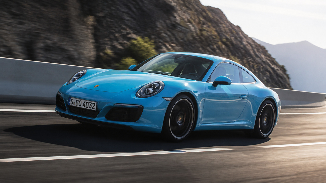 Carro esportivo azul Porsche 911 dirigindo em estrada de montanha sob luz do dia.