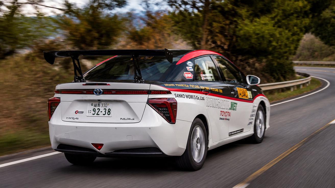 Carro de corrida Toyota branco com detalhes vermelhos e adesivos, em alta velocidade numa curva de estrada.