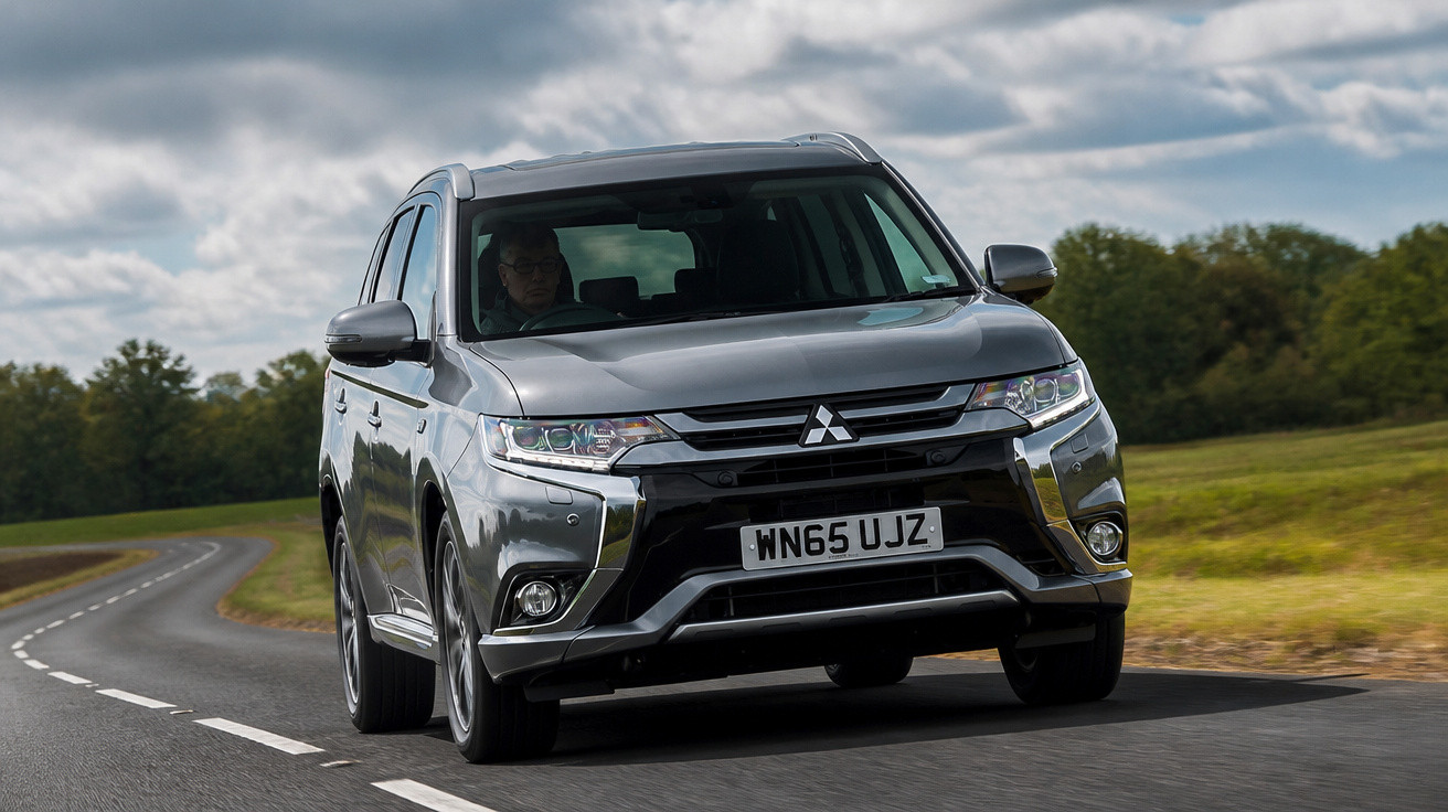 Carro SUV cinza da Mitsubishi dirigindo em estrada sinuosa com céu nublado e campo ao fundo.