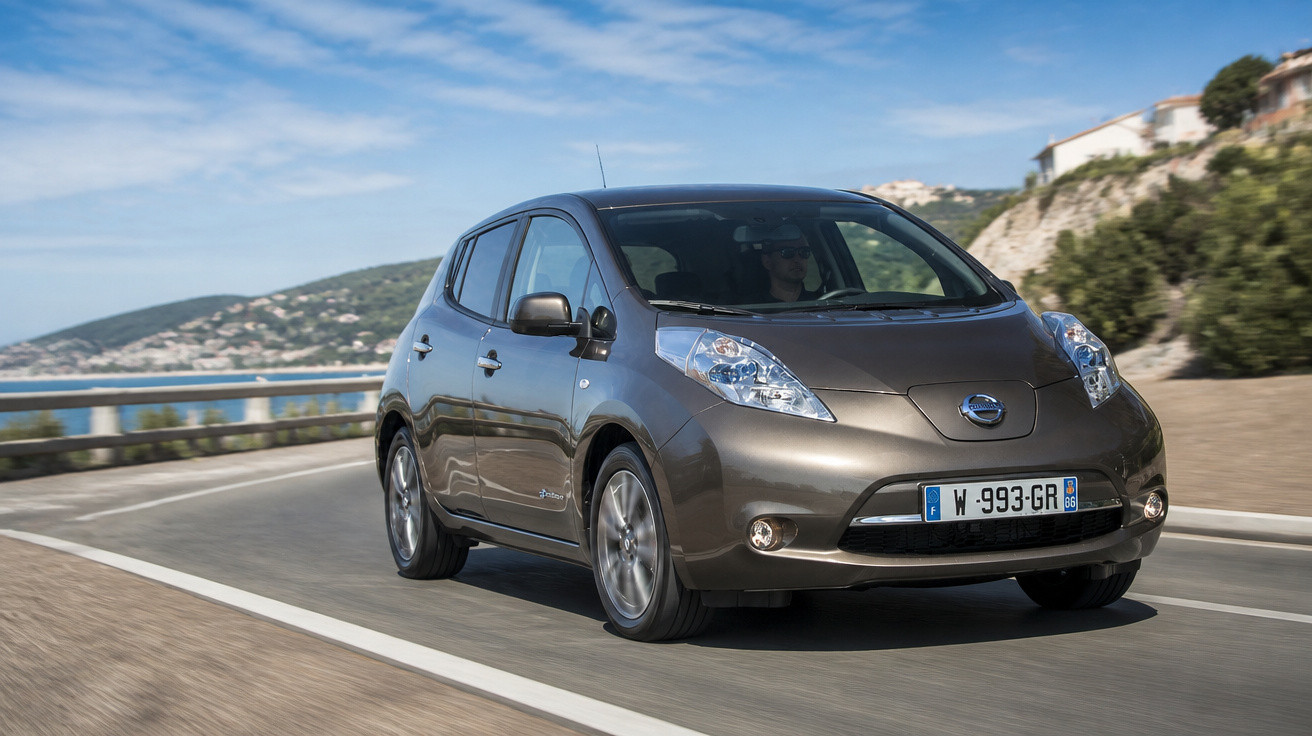 Carro elétrico cinza escuro modelo hatchback dirigindo em estrada costeira sob céu azul.