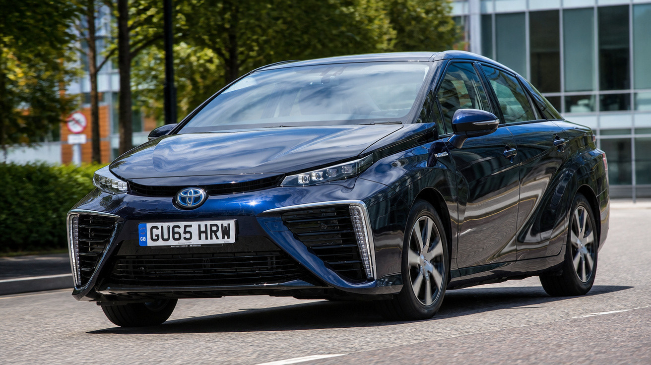 Carro Toyota azul escuro estacionado em rua urbana com edifícios ao fundo.