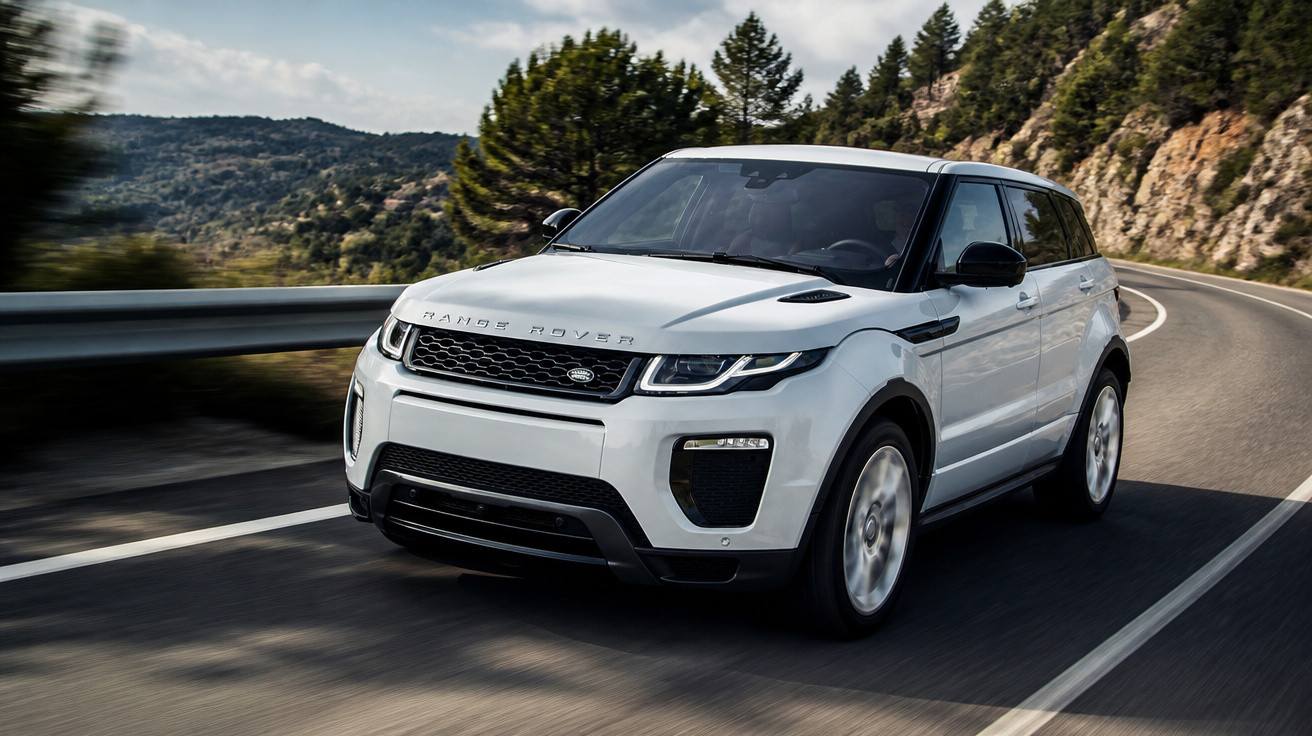 SUV branco Range Rover trafegando em estrada sinuosa cercada por árvores e montanhas.