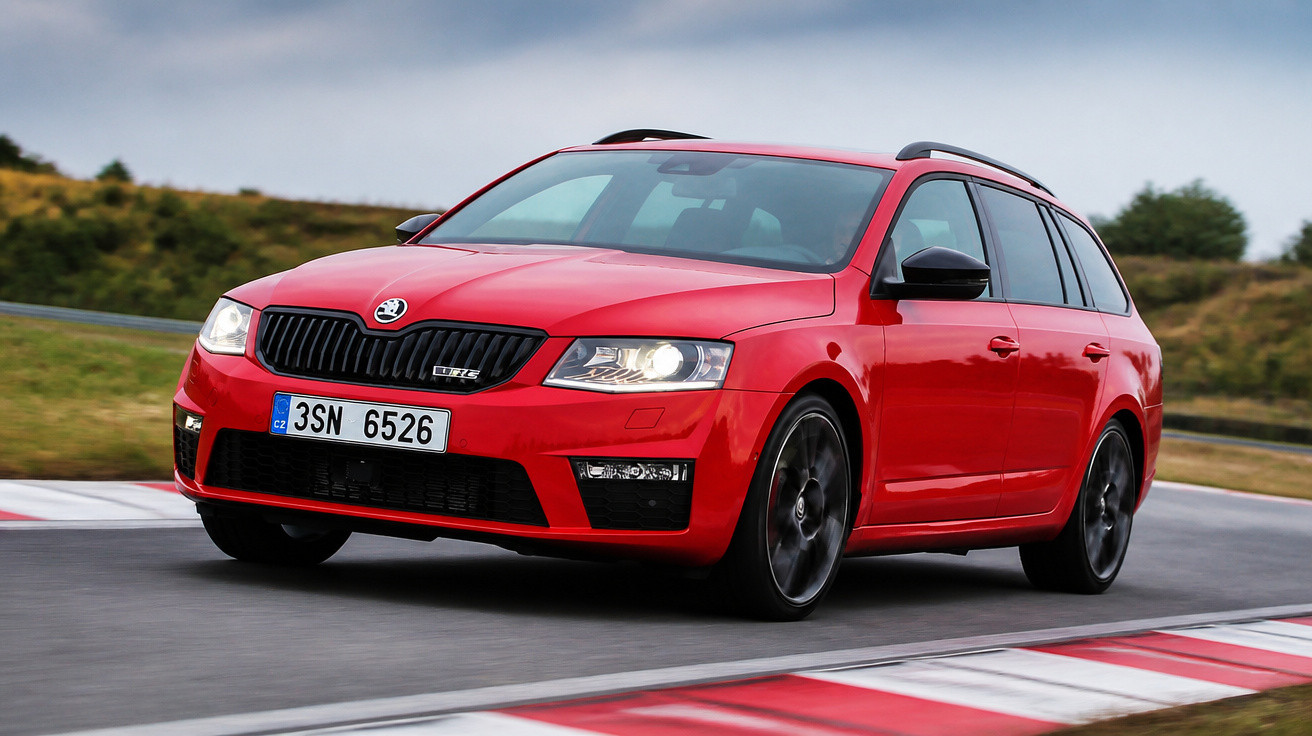 Carro vermelho modelo station wagon em alta velocidade em pista de corrida com curva e áreas verdes ao fundo.