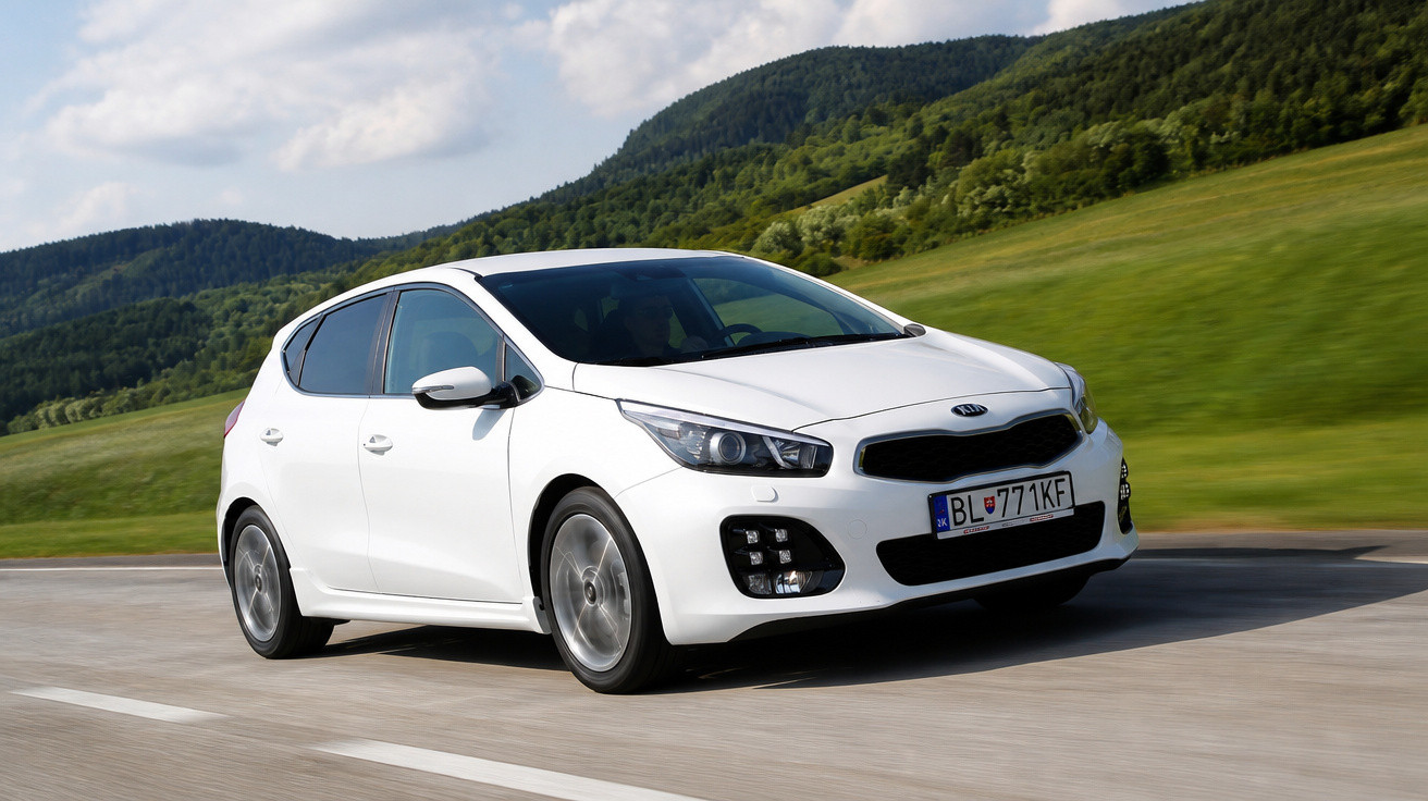 Carro branco Kia hatchback em movimento em estrada com colinas verdes ao fundo e céu parcialmente nublado.