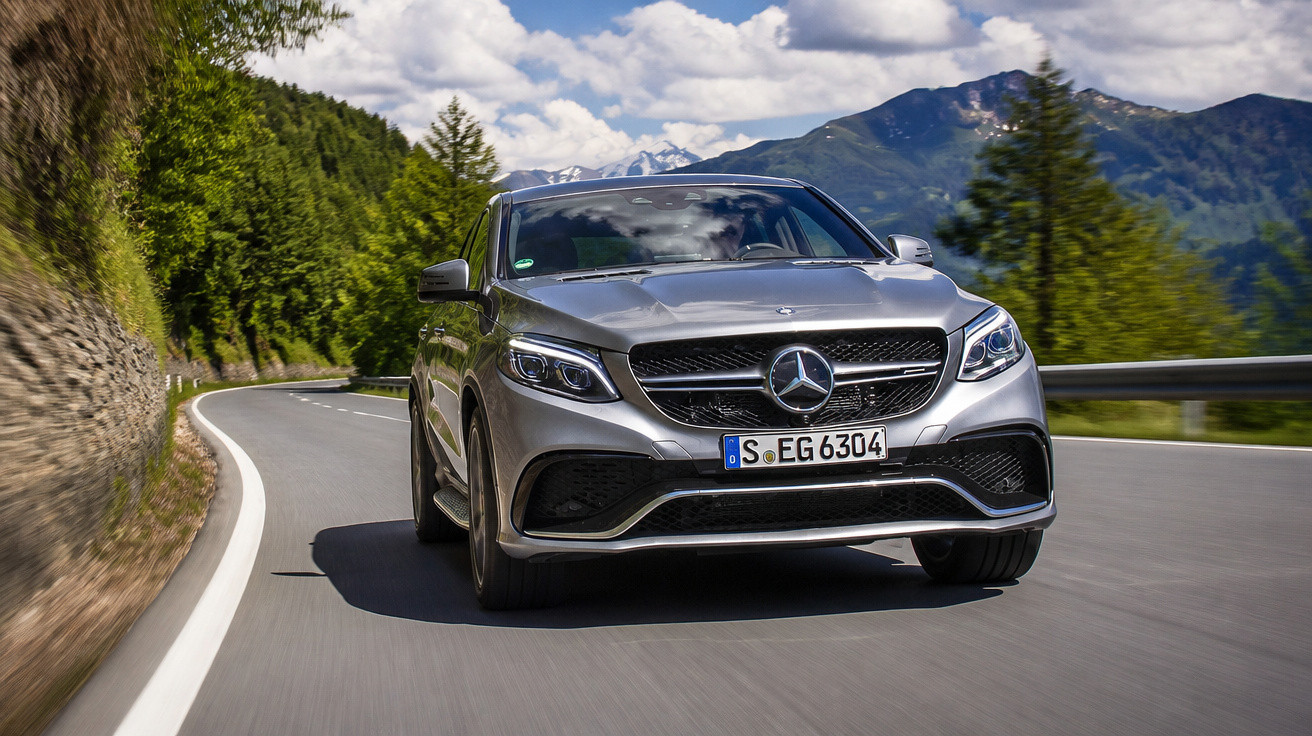 Carro Mercedes-Benz cinza circulando em estrada sinuosa com montanhas e árvores ao fundo.