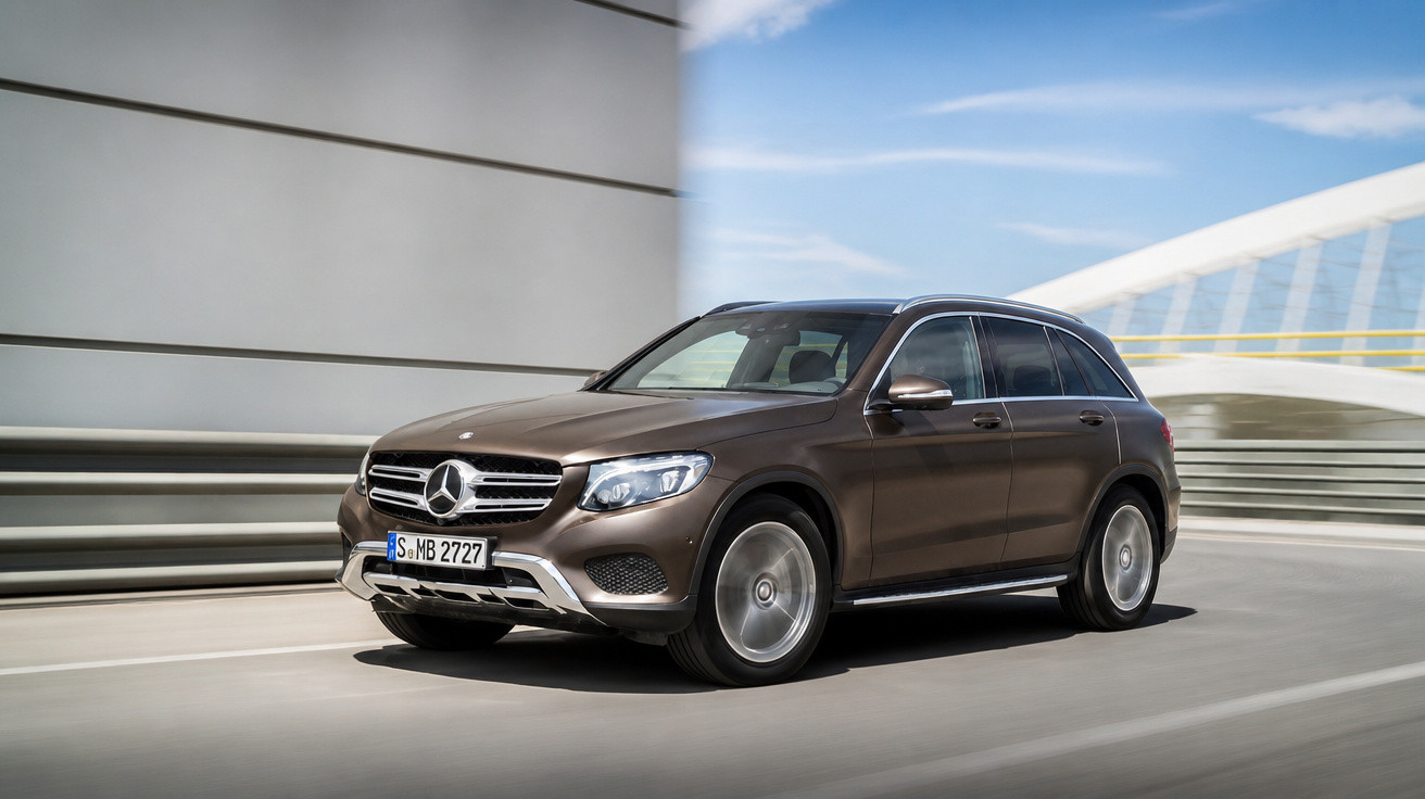 Carro SUV Mercedes-Benz marrom em movimento em uma estrada urbana com edifícios modernos ao fundo.