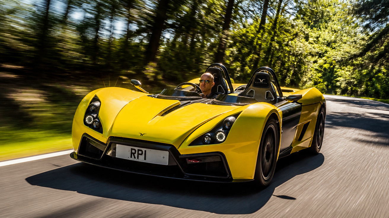 Carro esportivo amarelo aberto com motorista, em estrada sinuosa cercada por árvores iluminadas pelo sol.
