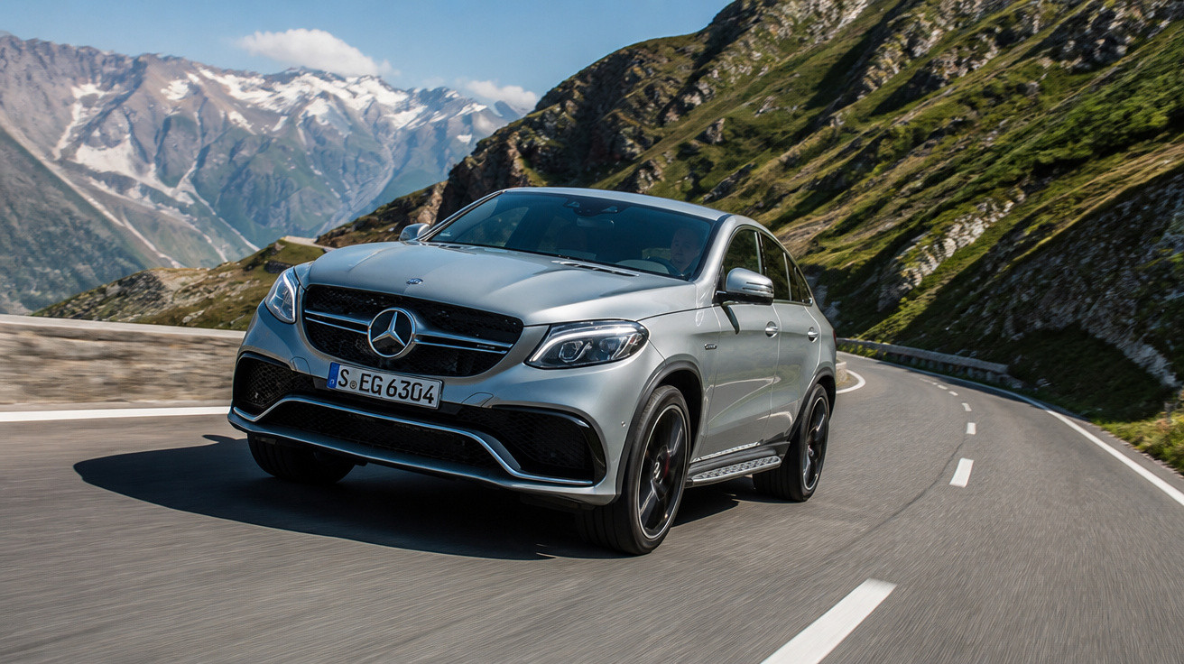 Carro Mercedes-Benz SUV prata dirigindo em estrada sinuosa nas montanhas com céu azul e neve ao fundo.