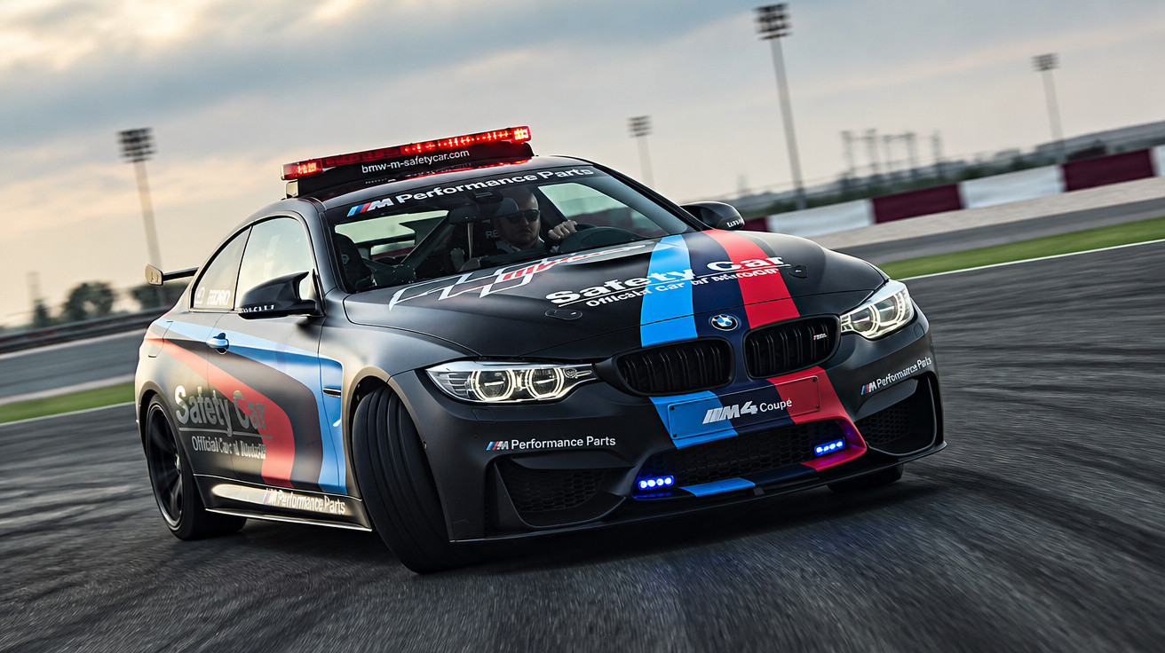 Carro BMW M4 Safety Car em pista de corrida com luzes de emergência acionadas ao entardecer.