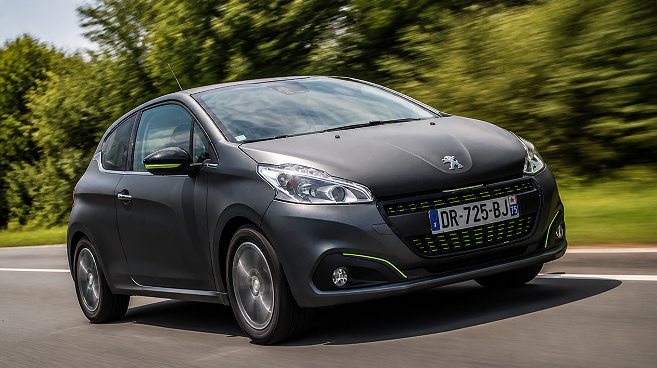 Carro preto Peugeot em movimento em estrada com árvores e céu nublado ao fundo.