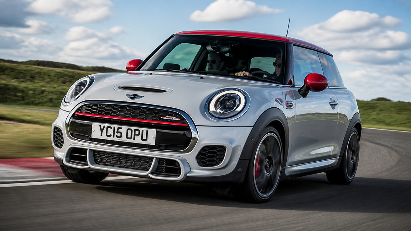 Carro Mini Cooper branco com teto e retrovisores vermelhos em curva de pista de corrida.