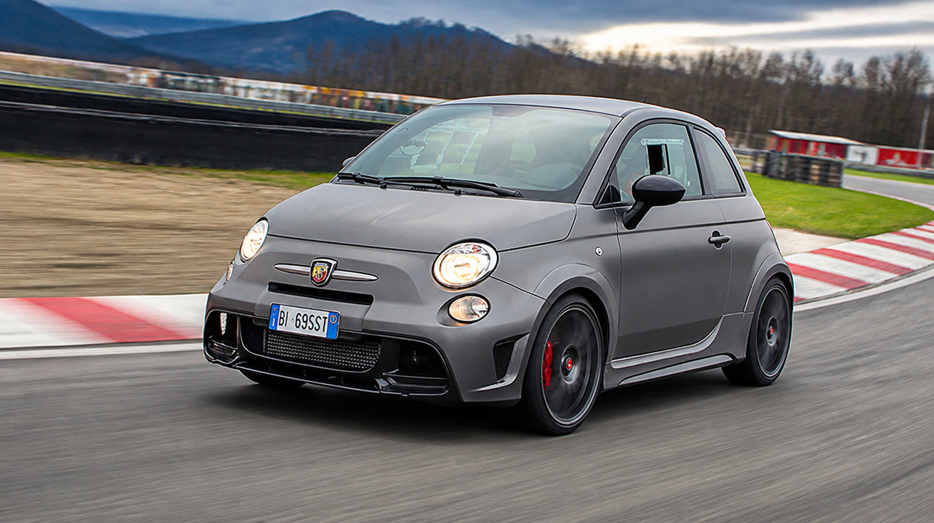 Carro esportivo compacto cinza em curva de pista de corrida com rodas pretas em movimento.