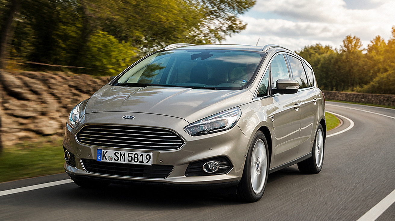 Carro Ford prata cinza em estrada curva com árvores e céu nublado ao fundo.