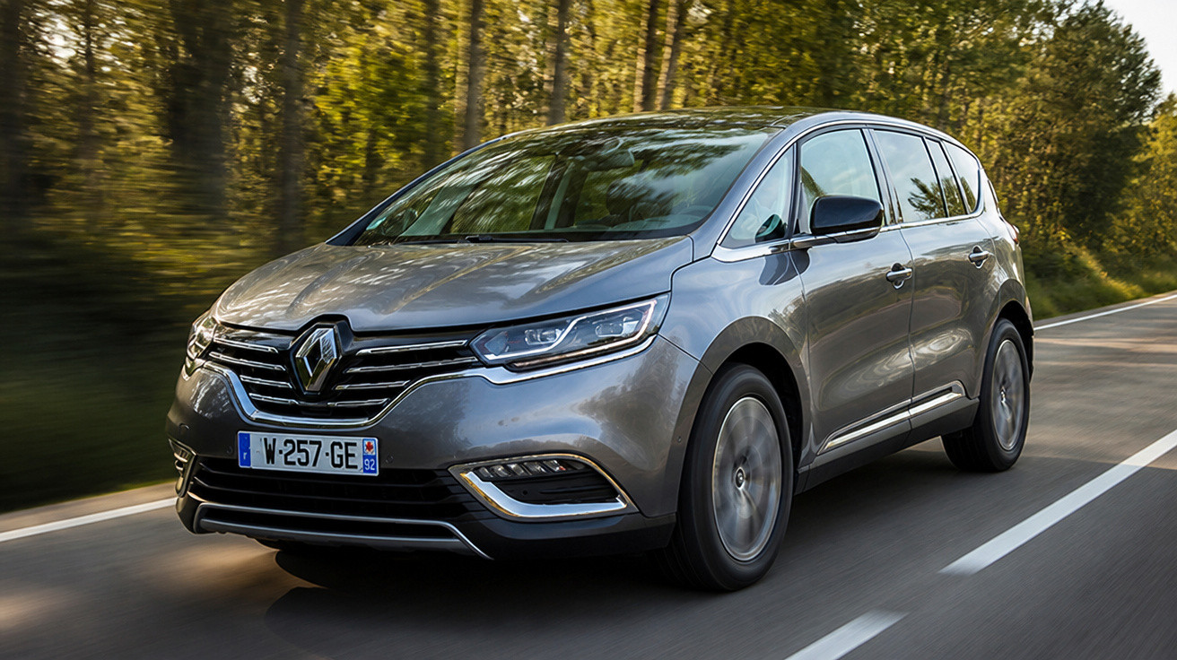 Carro cinza Renault em movimento em estrada rodeada de árvores ao entardecer.