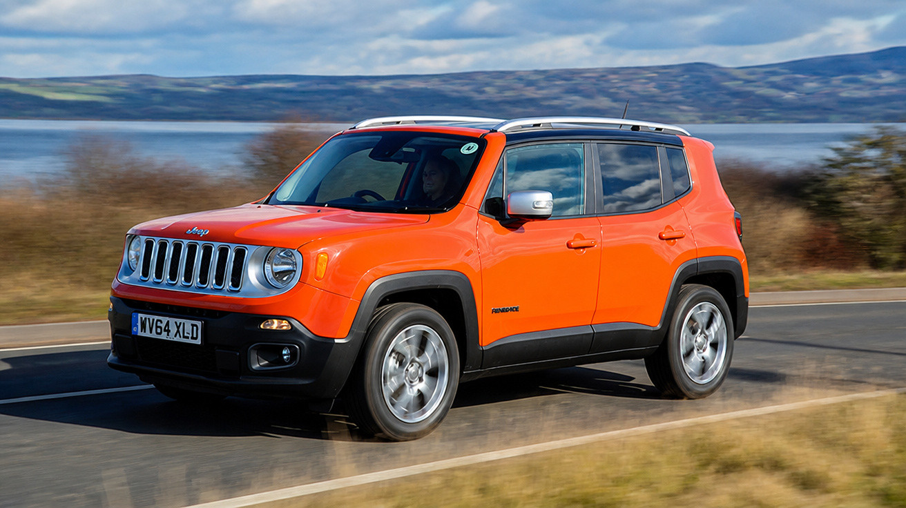 SUV Jeep Renegade laranja trafegando em estrada com lago e morros ao fundo.