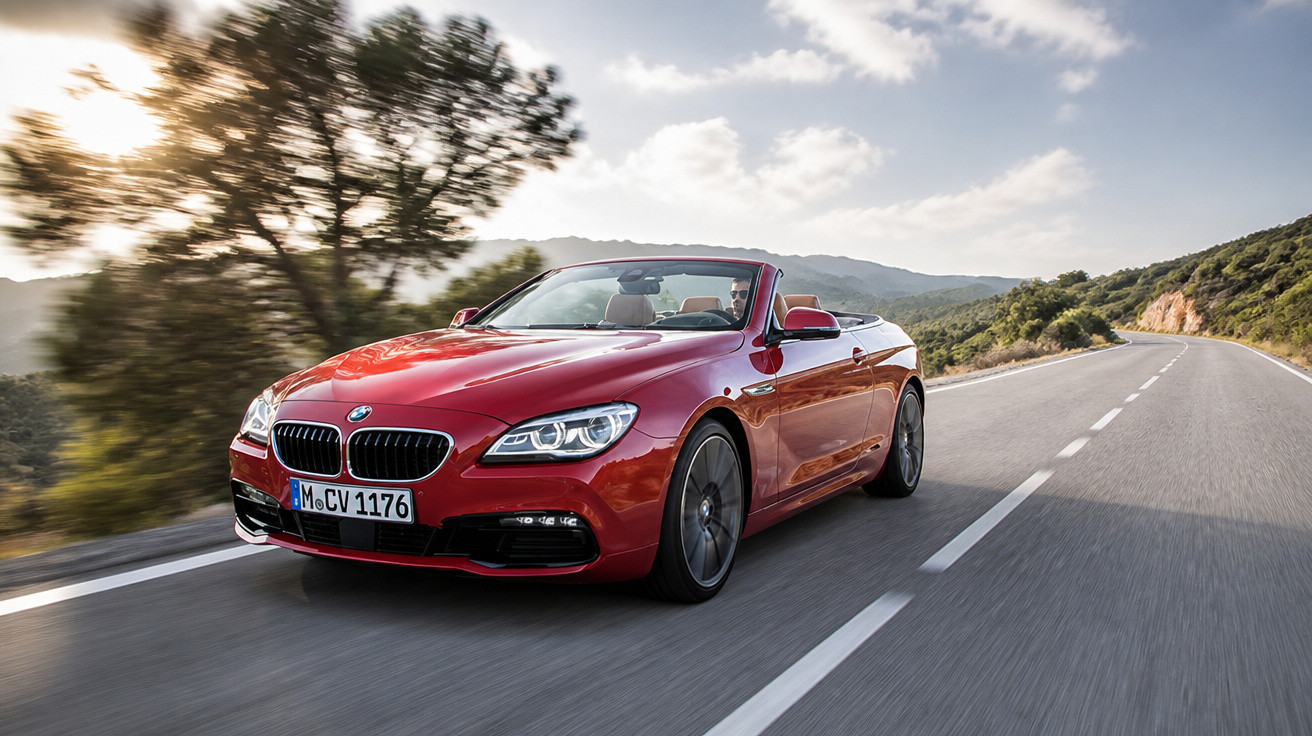 Carro conversível vermelho BMW em alta velocidade em estrada cercada por árvores e montanhas ao pôr do sol.